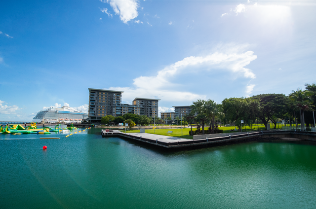 Waterfront scene with teal water, buildings, a cruise ship, and a sunny blue sky.