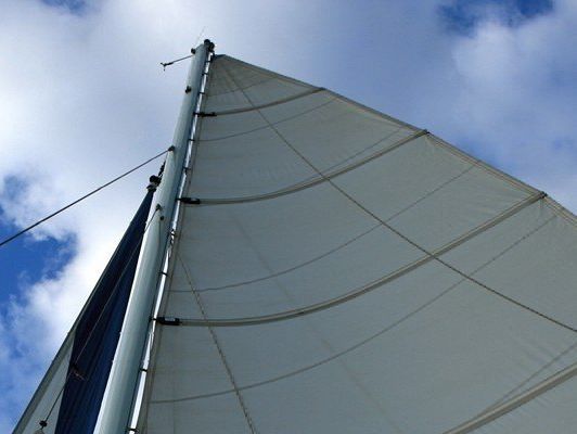 White sail of a sailboat, against a blue sky with fluffy clouds.