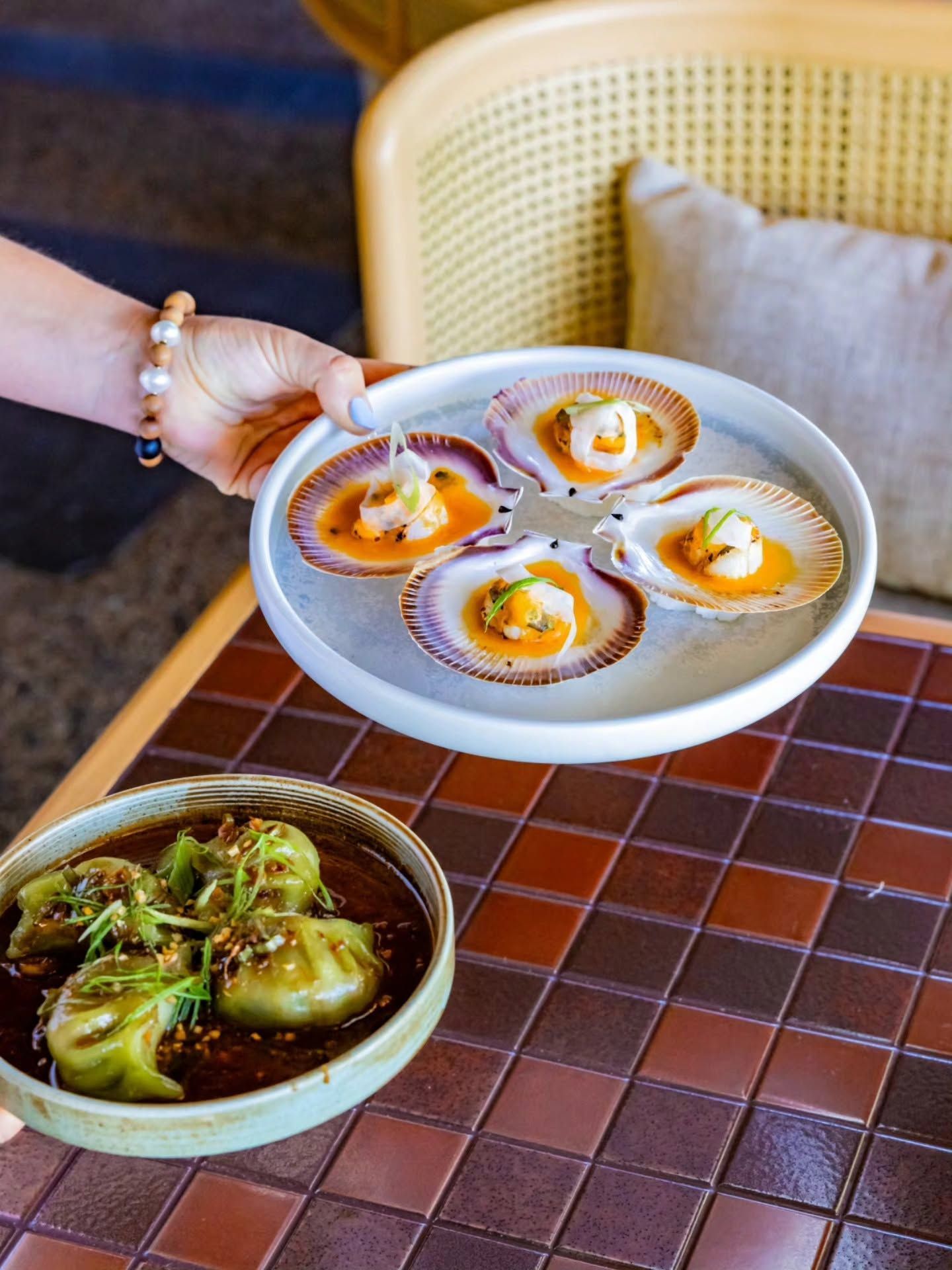 Plate of scallops being carried to alfresco dining table with mushroom dumplings.