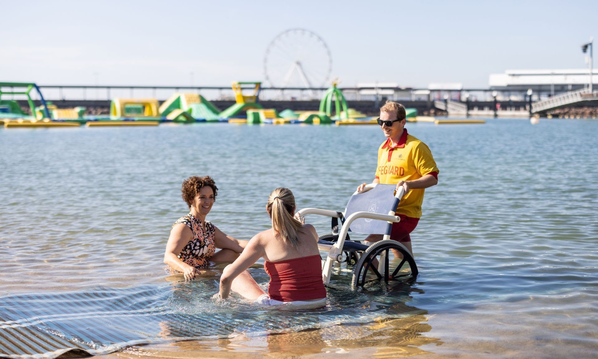 Lifeguard holding aquatic wheelchair, two women sit in the water. The words 'Recreation Lagoon' are written over the image.