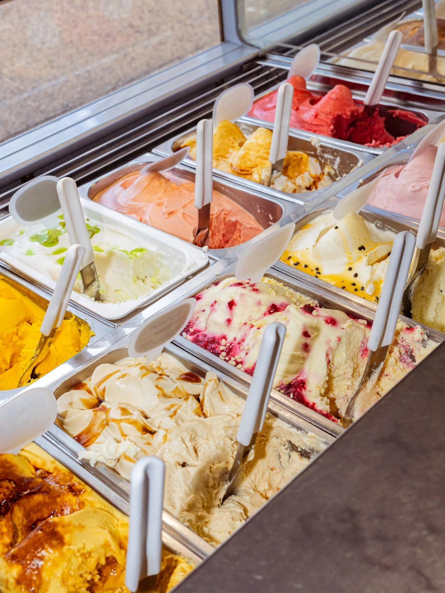 Gelato display case with various flavors and serving spoons.
