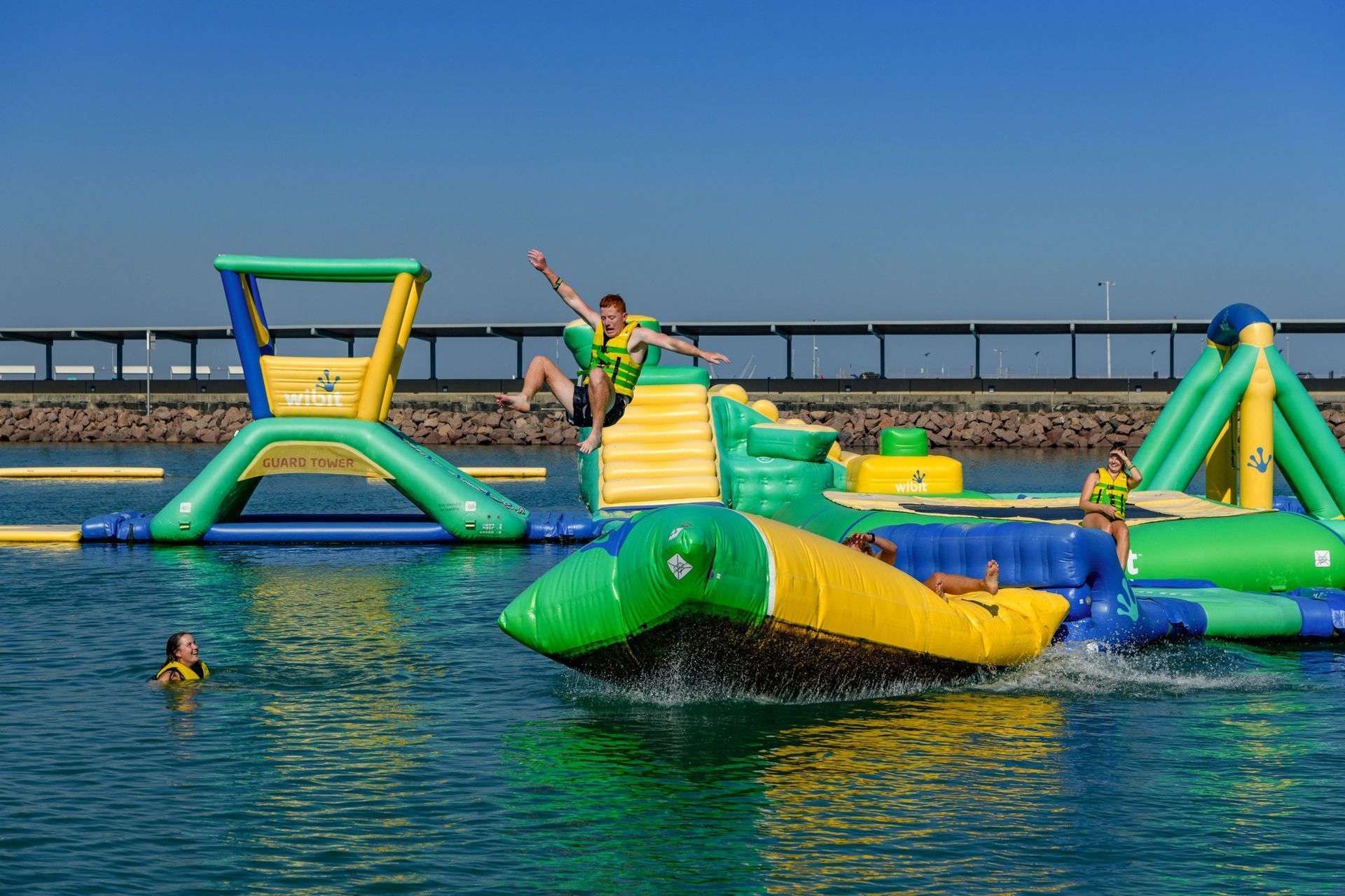 People playing on an inflatable water park in a blue lake. Sunny day.