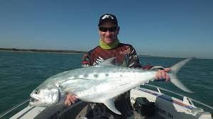 Man holding a large, silver fish on a boat; ocean in the background.