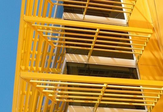 A yellow fire escape on the side of a building against a blue sky.