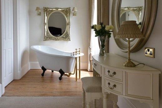 Elegant bathroom with a freestanding tub, ornate mirror, and cream vanity by a window