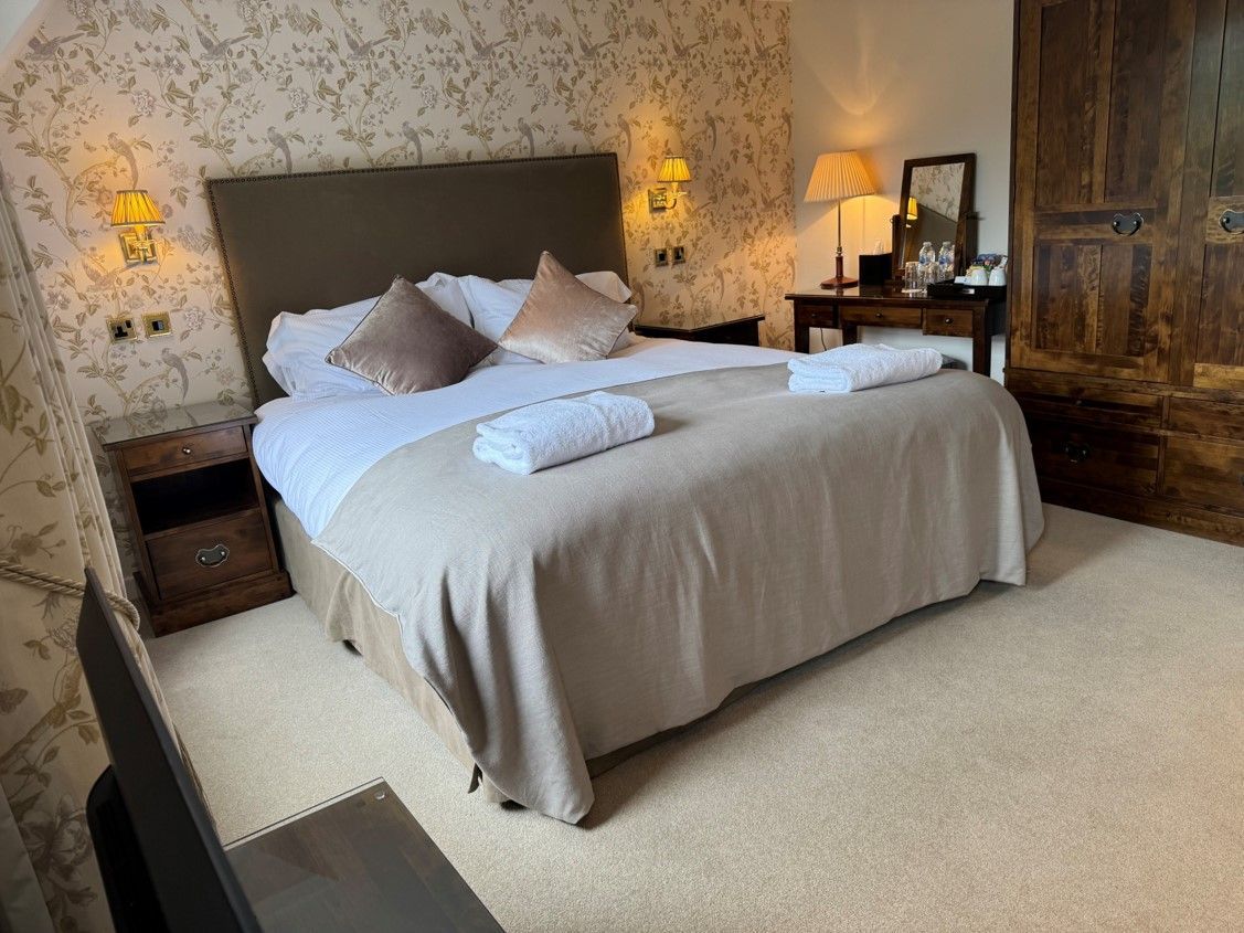 Cozy bedroom with a large bed, beige bedding, bedside lamps, and floral wallpaper
