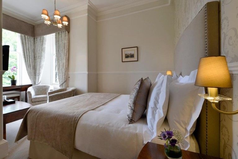 Cozy bedroom with a neatly made bed, bedside lamp, armchair, and large window with curtains