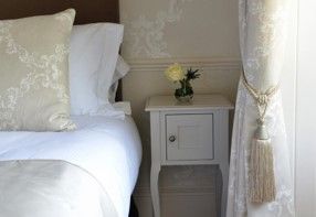 Cozy bedroom with a white bed, bedside table, flowers, and sheer curtain with tassel tieback