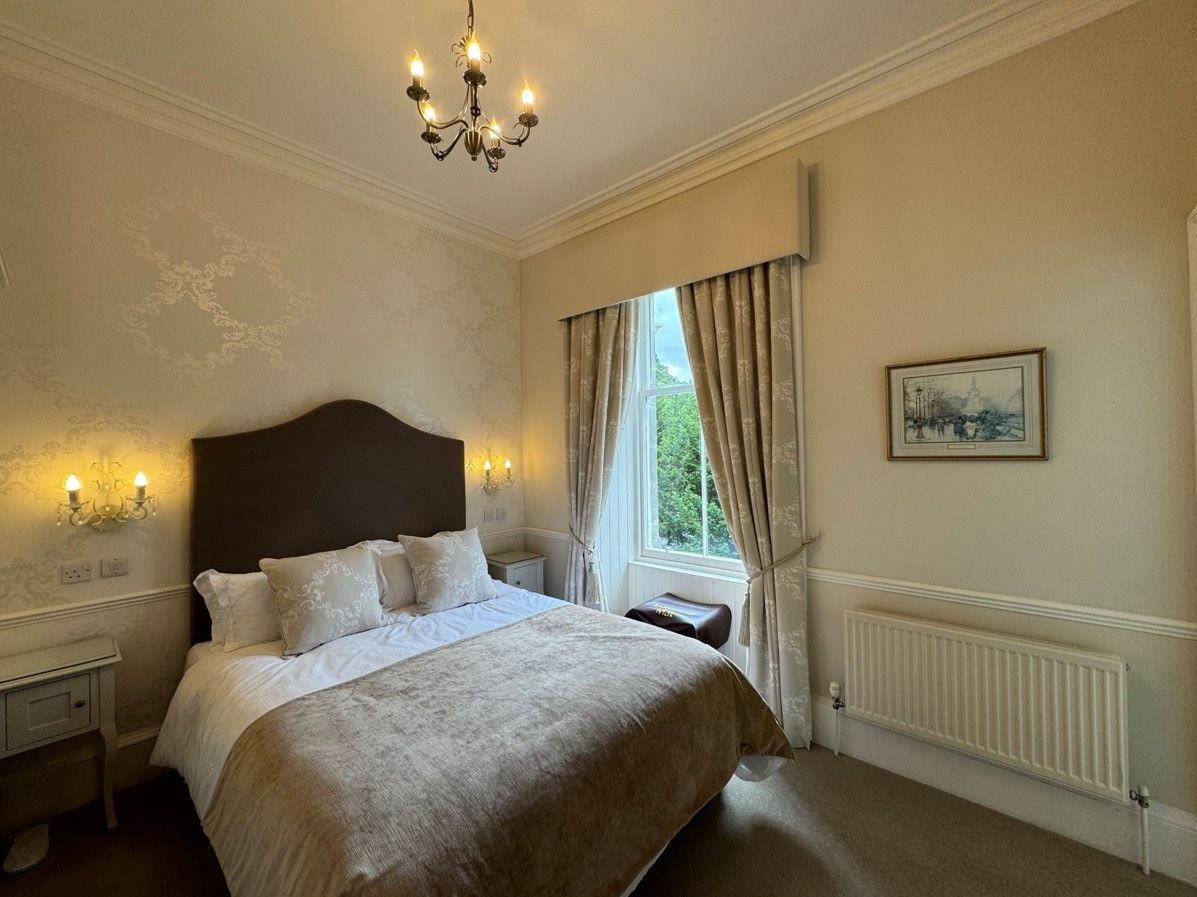Bright, elegant bedroom with a double bed, cream walls, window, and radiator