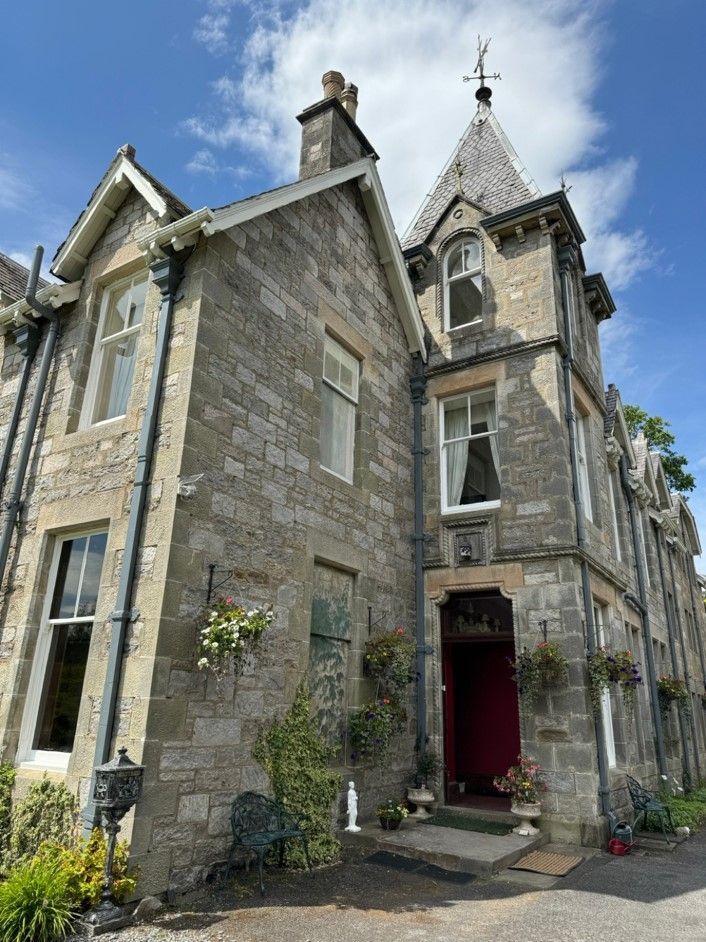Stone Victorian house with turret, tall windows, and a red front door beneath a blue sky