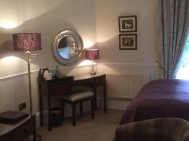 Cozy bedroom with a vanity table, round mirror, lamps, framed art, and a bed by the window.