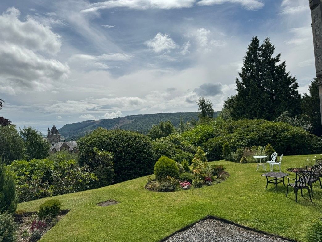 Lush garden lawn with flowers, chairs, and a cloudy mountain view in the distance