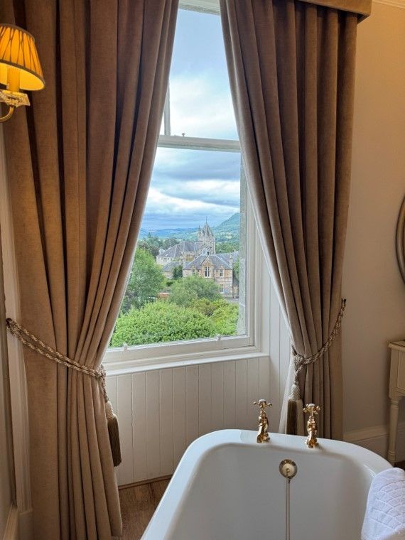 Elegant bathroom with clawfoot tub, brown curtains, and a window view of a coastal city and water