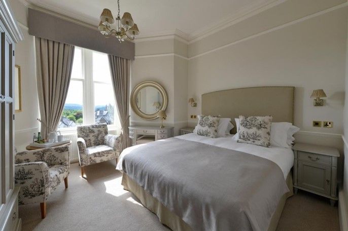 Elegant bedroom with a large bed, floral chairs by a window, and soft beige decor.