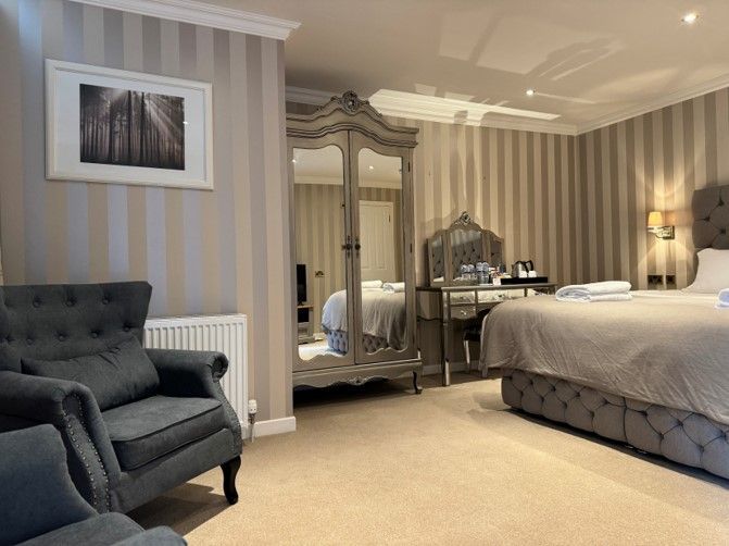 Elegant bedroom with tufted armchair, ornate mirror, bed, bedside lamp, and striped wallpaper