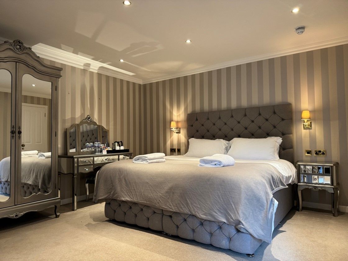 Elegant bedroom with tufted gray bed, striped wallpaper, mirrored wardrobe, and soft bedside lamps