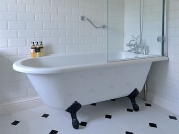 Clawfoot bathtub in a white tiled bathroom with a glass shower screen and black-and-white floor tiles