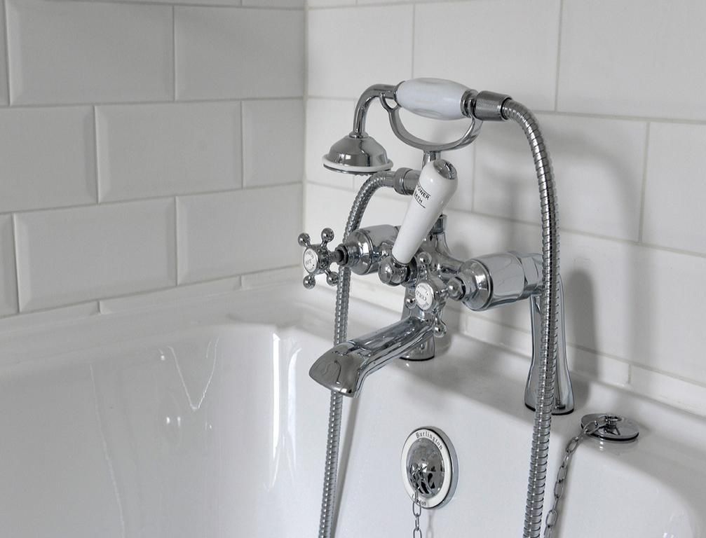 Bathroom tub with chrome faucet and handheld showerhead against white tile wall