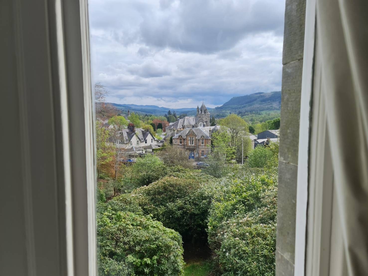 View through curtains of a hillside village and distant mountains under cloudy skies