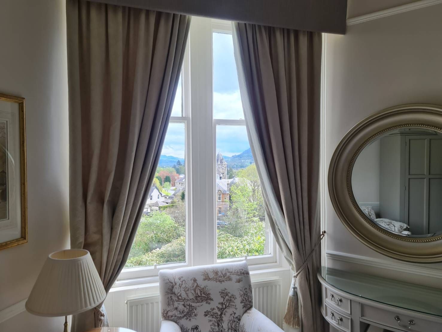 Bright room with a window, beige curtains, and a round mirror above a mantelpiece.