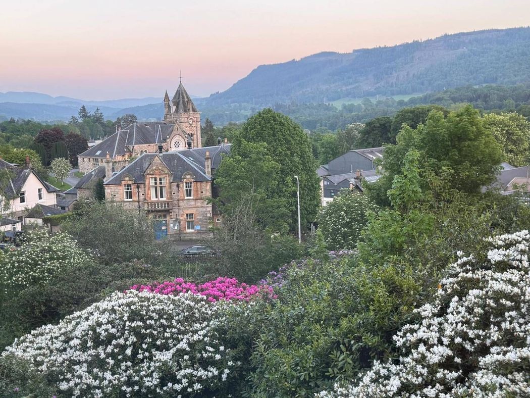 Historic stone buildings amid lush garden flowers with mountains in the background at dusk