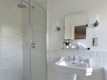 Bright white bathroom with glass shower, pedestal sink, mirror, and wall sconces
