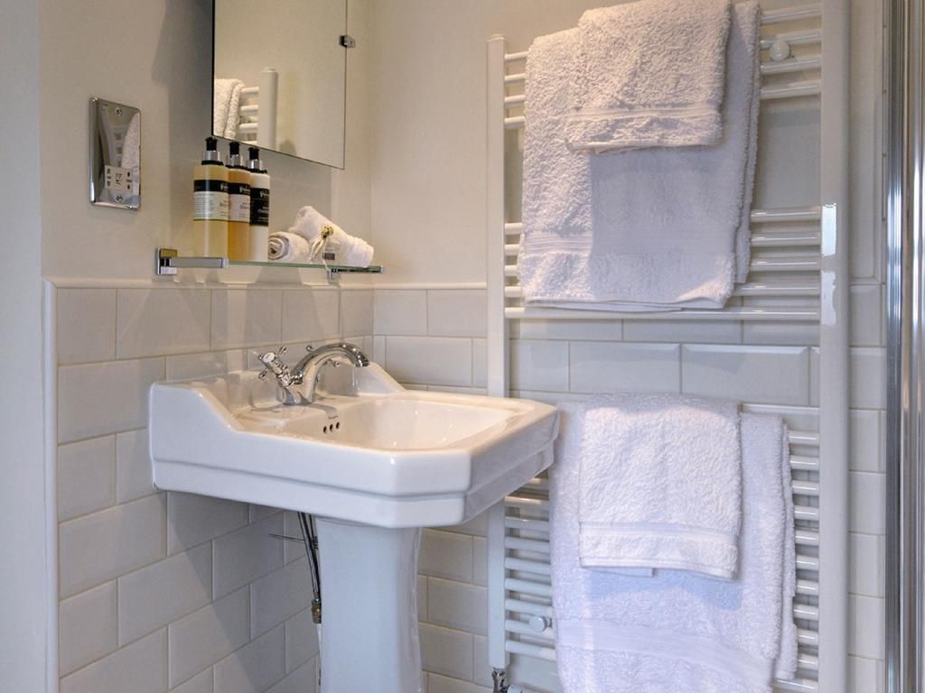 Small white bathroom with wall-mounted sink, mirror, and towel rack with folded white towels.