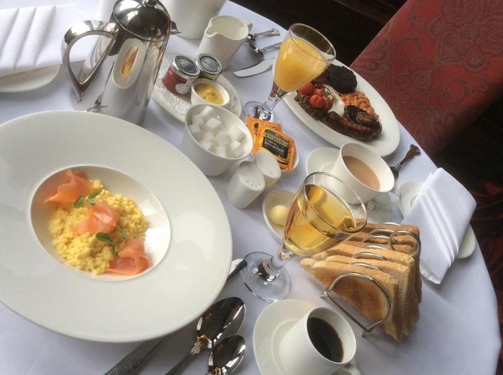 Breakfast table with eggs, toast, fruit, coffee, tea, and orange juice on white linens