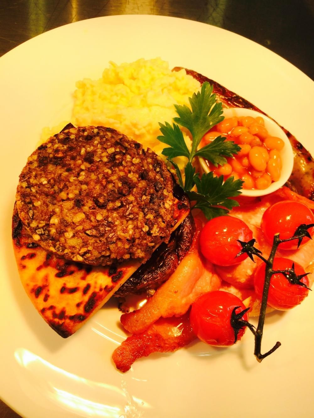 Plated breakfast with haggis, scrambled egg, cherry tomatoes, and parsley garnish on a white plate. A typical breakfast in SCotland or a Full Scottish Breakfast