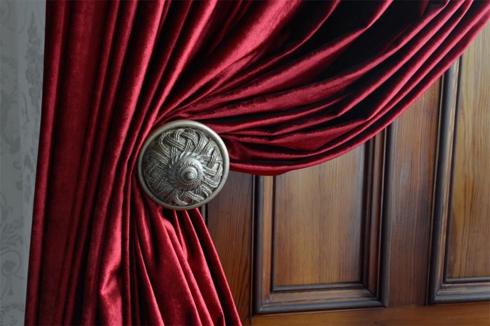 Red velvet curtain with a silver medallion tied over a wooden paneled door