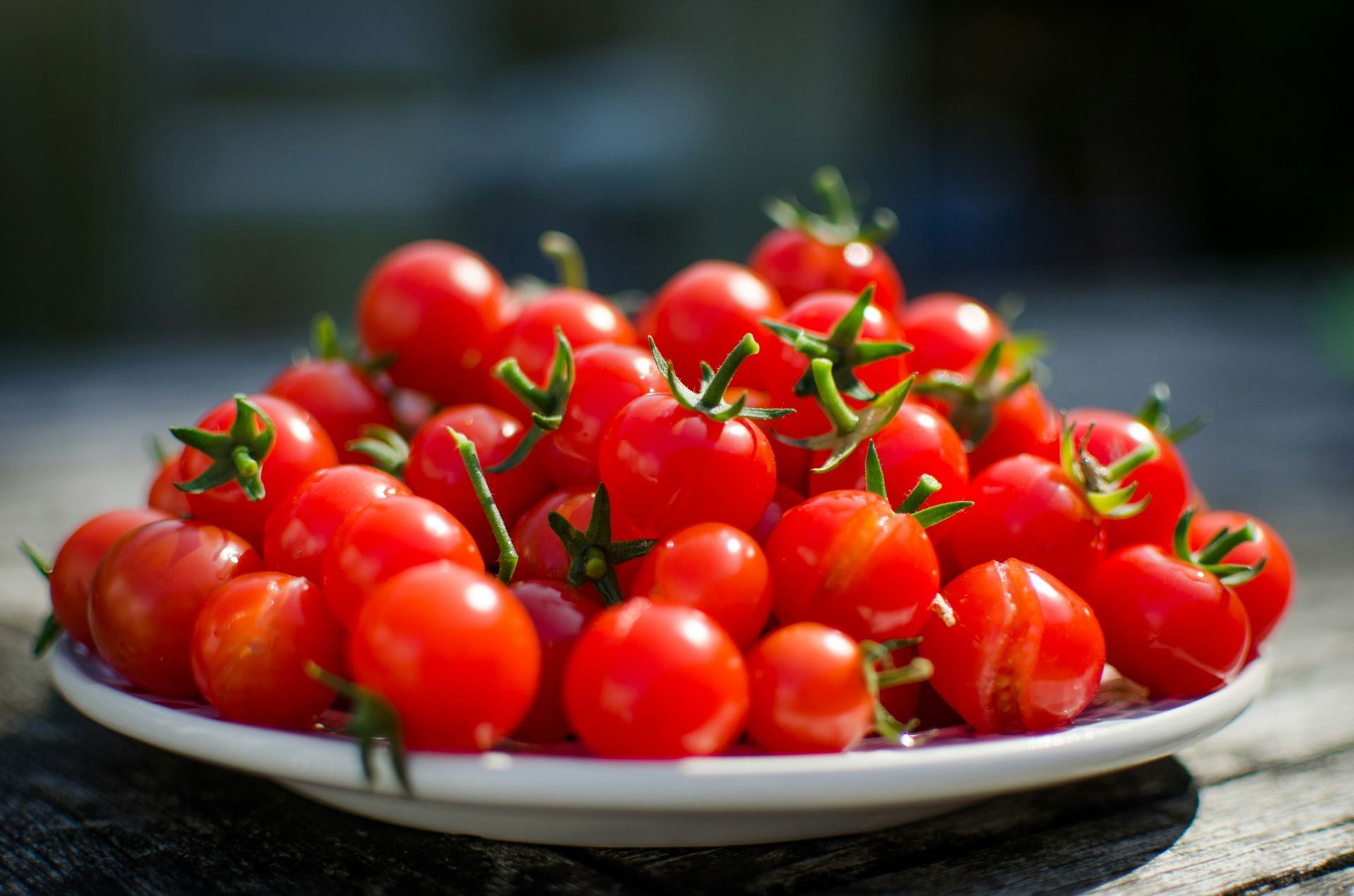 Plate piled with red cherry tomatoes, fresh and glossy outdoors on a table