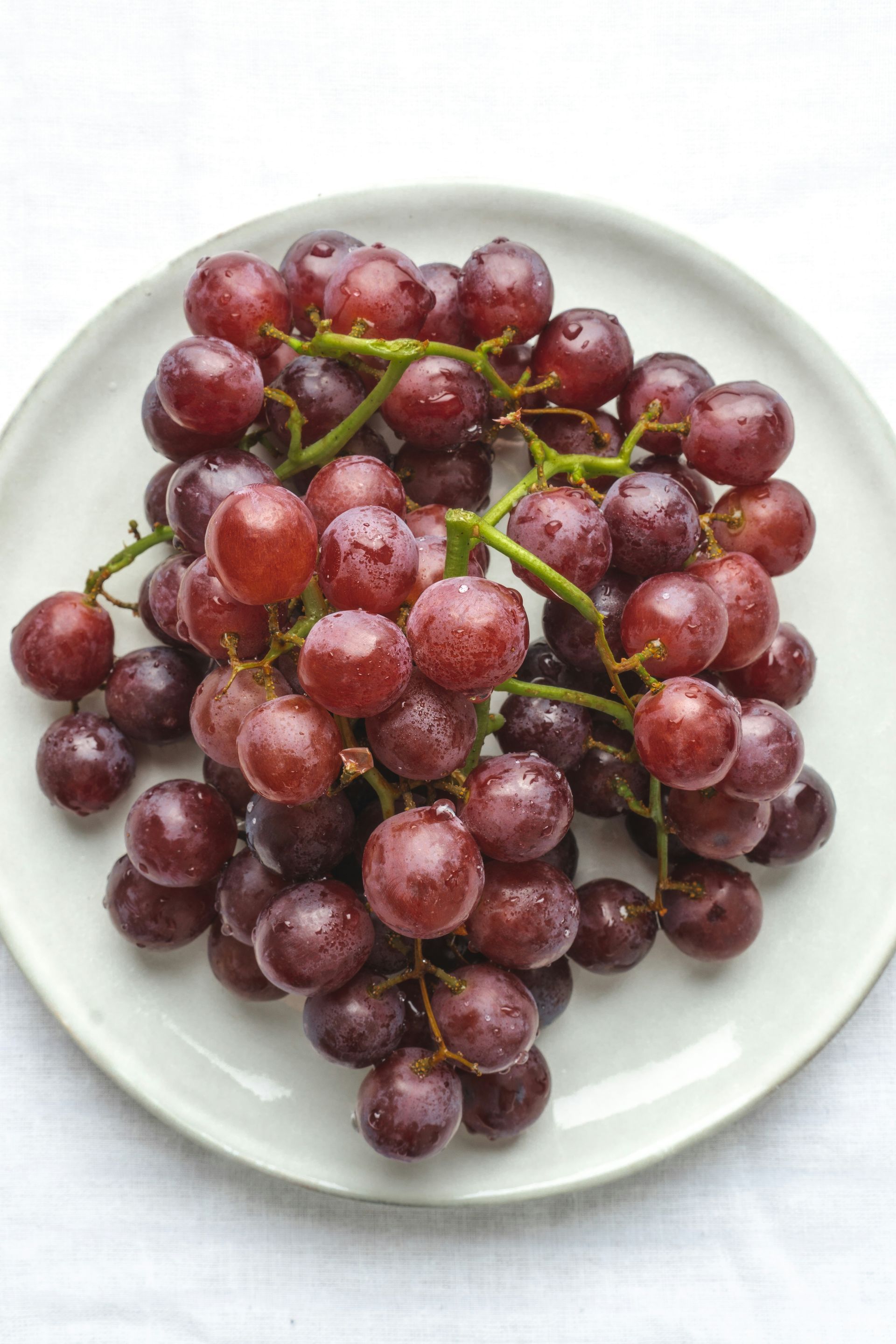 A white plate piled with red grapes on a white background