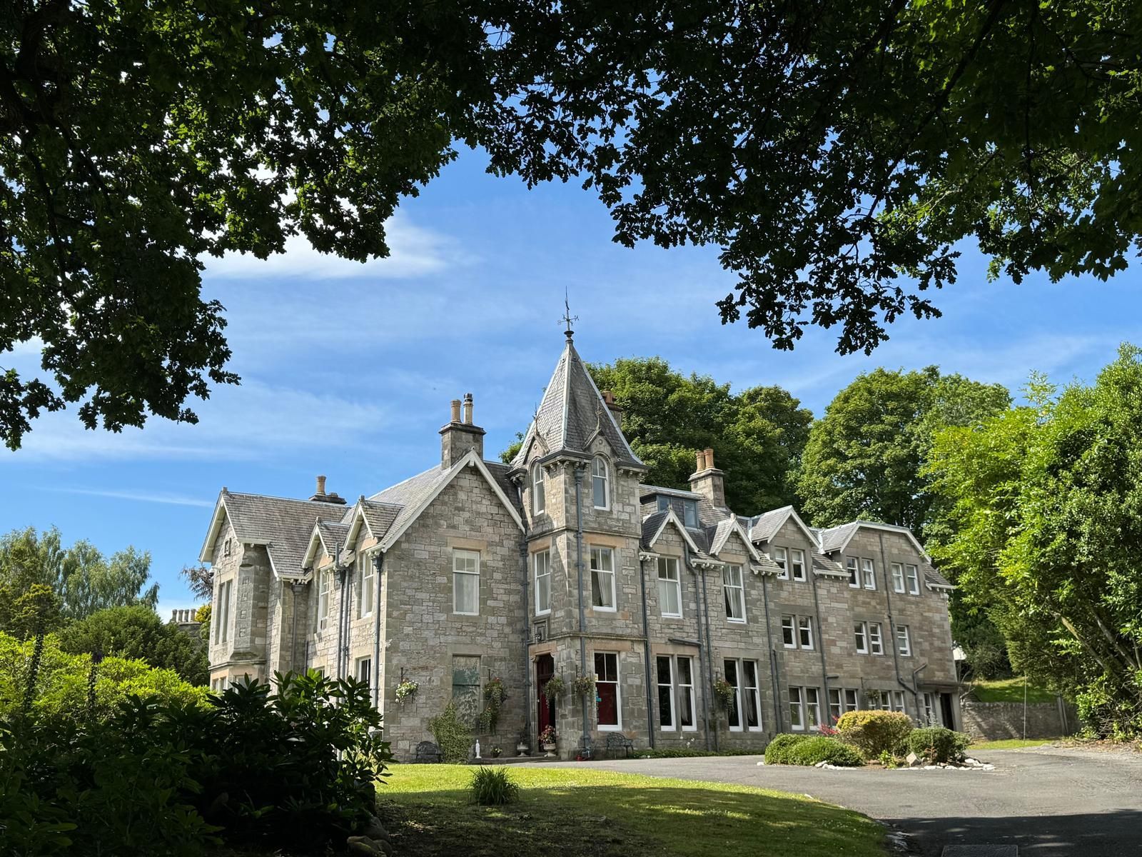 Stone manor house surrounded by trees under a blue sky