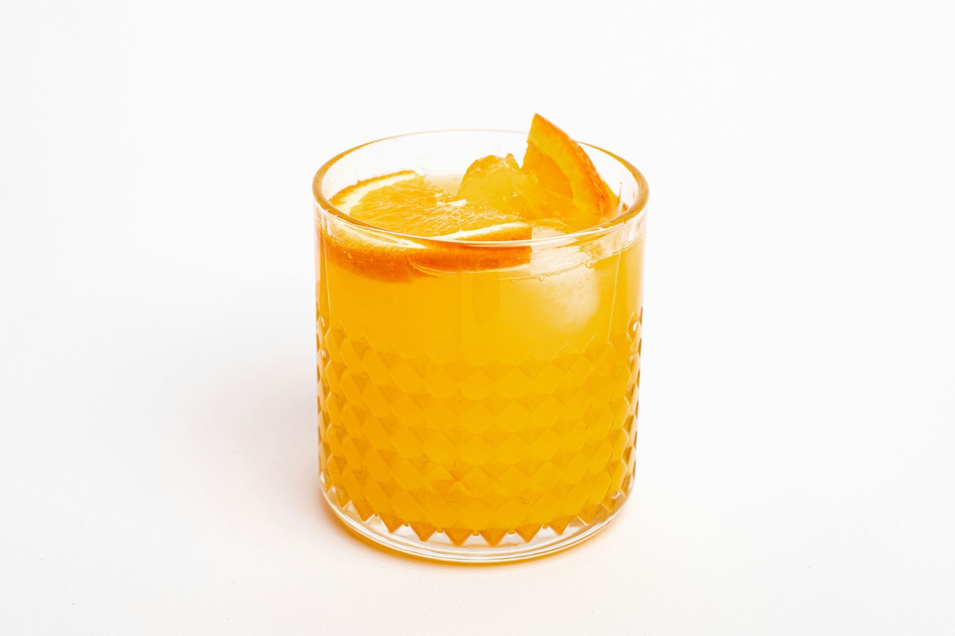 Orange juice in a textured glass with an orange slice garnish on a white background