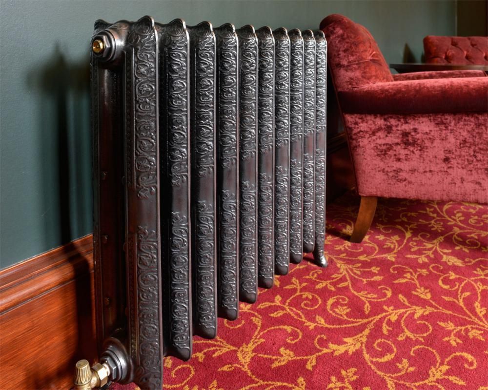 Black radiator beside a red velvet sofa on a patterned red carpet in a living room