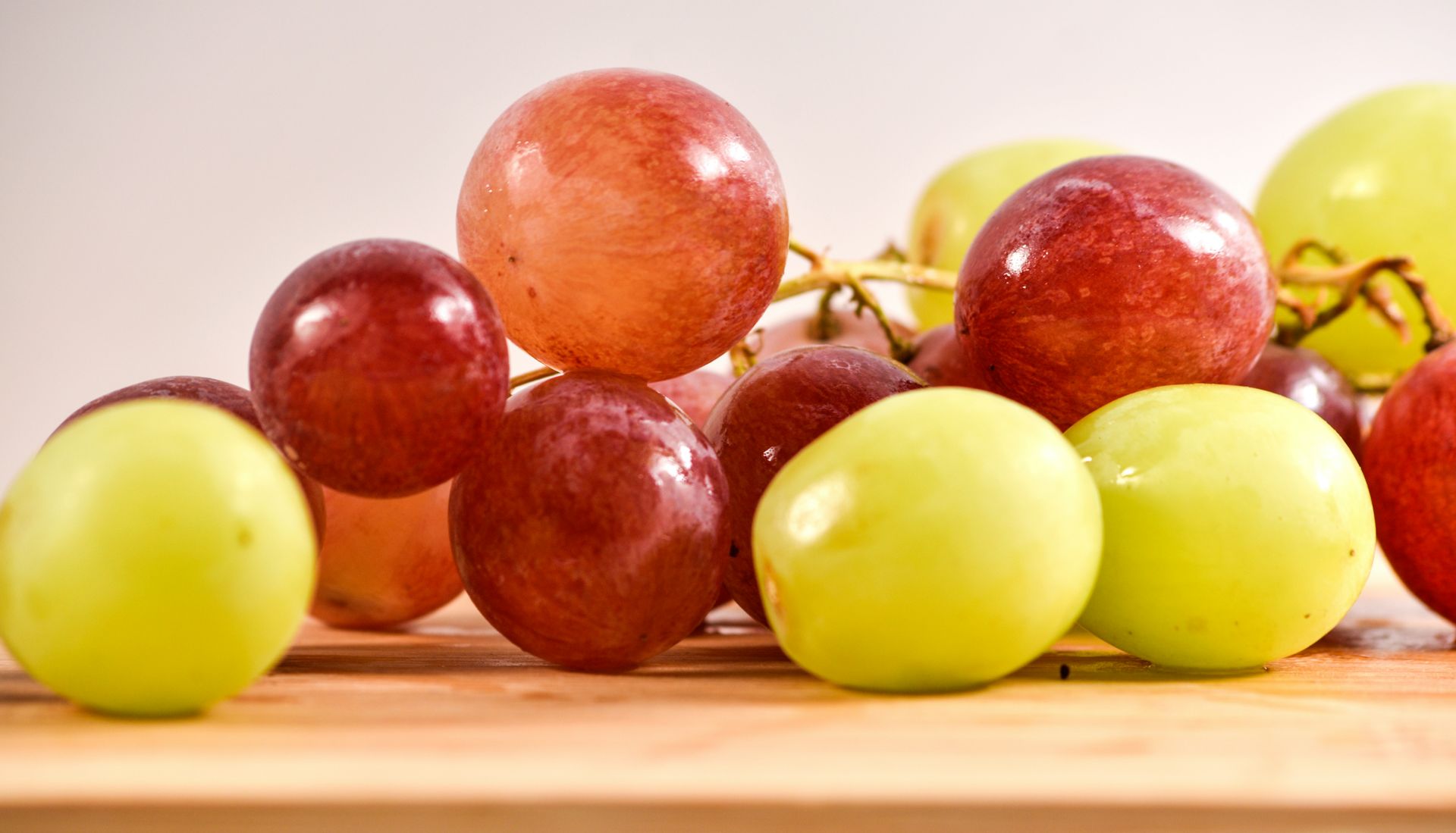 Mixed red, green, and golden grapes piled on a wooden surface