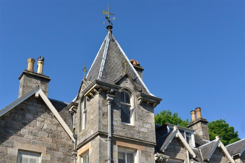 Stone building with a steep slate roof and tower against a clear blue sky