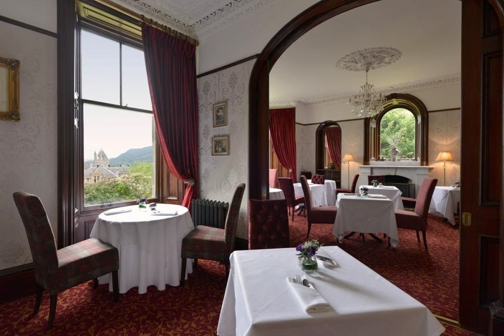 Elegant dining room with round tables, red carpet, and large windows overlooking a scenic view