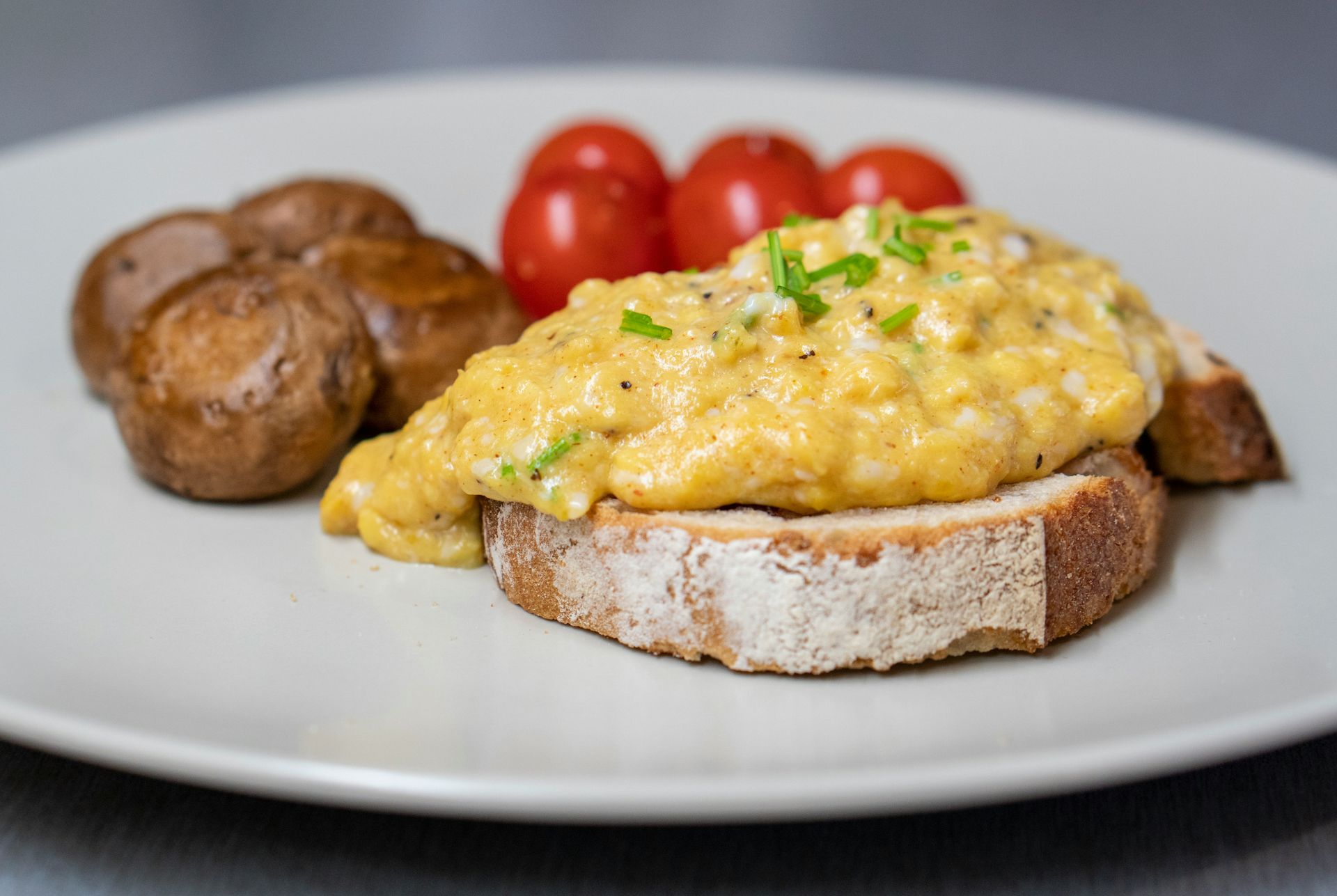 Scrambled eggs on toast with mushrooms and cherry tomatoes on a white plate