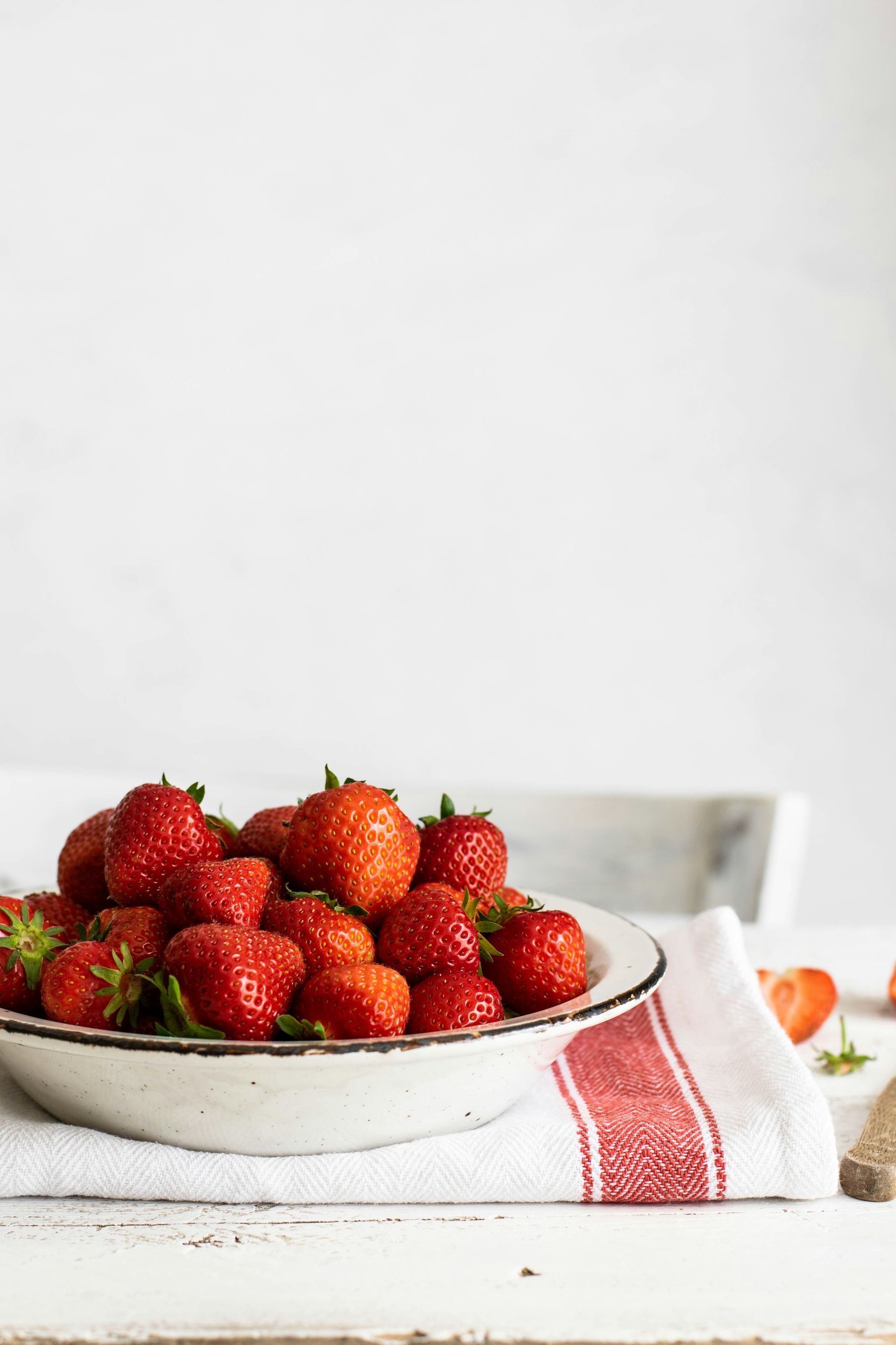 Bowl of fresh strawberries on a white tablecloth with a red-striped napkin