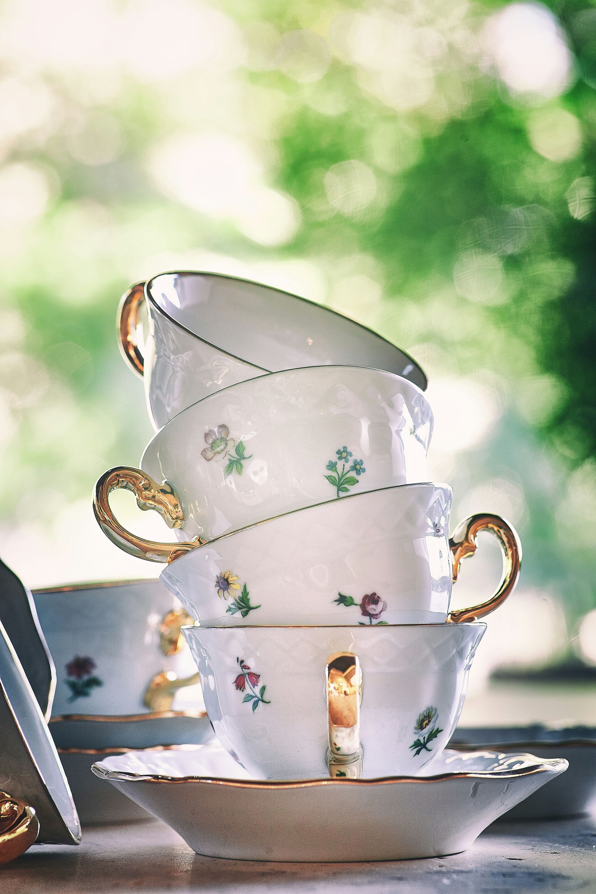 Stacked floral teacups on saucers against a bright, blurred garden background