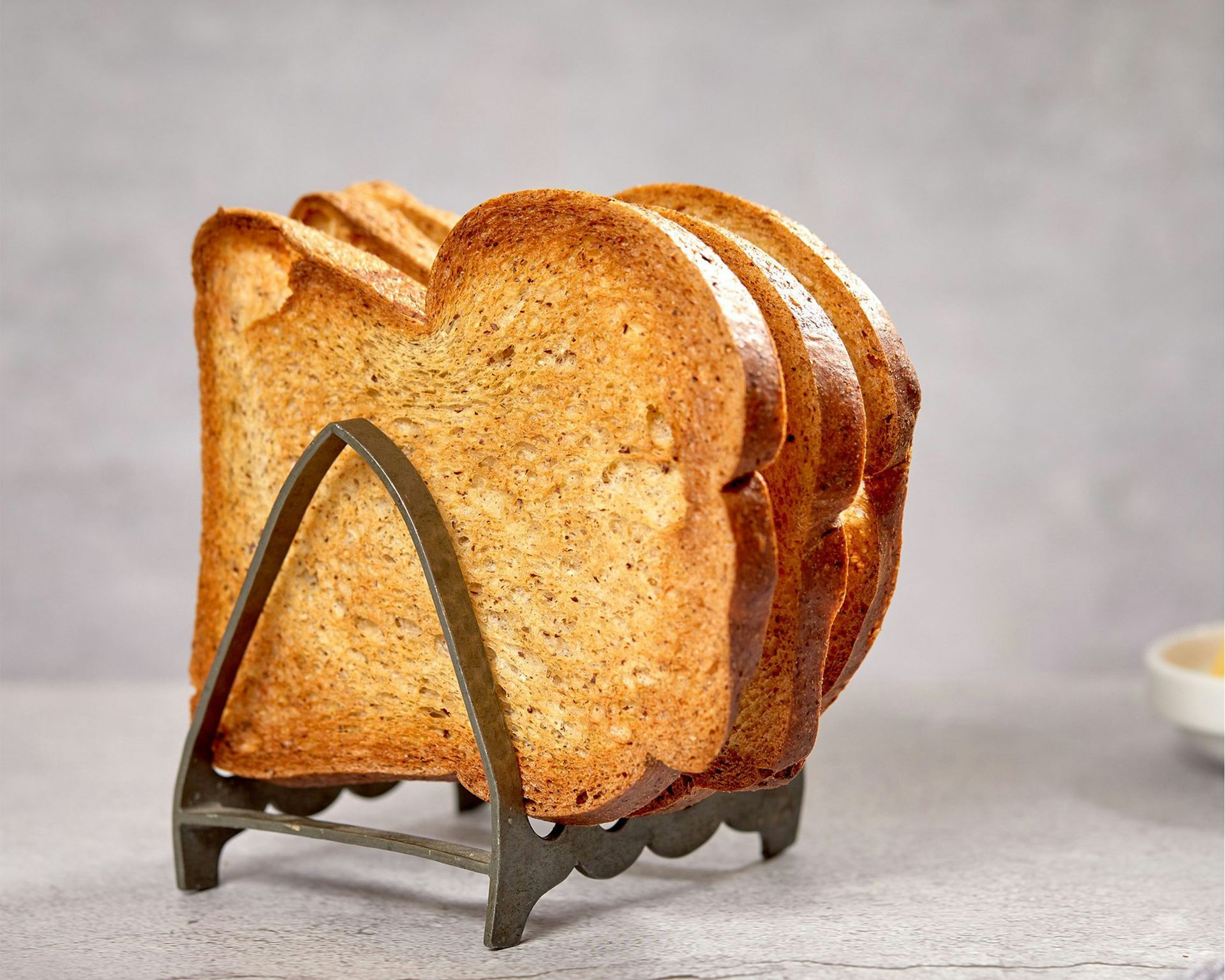 Sliced loaf of golden-brown bread on a metal stand against a gray background