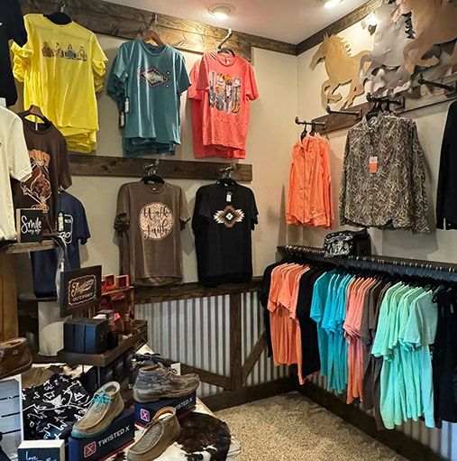 Clothing store interior with t-shirts, shirts, and accessories. Wooden and corrugated metal accents, and cowhide rug.