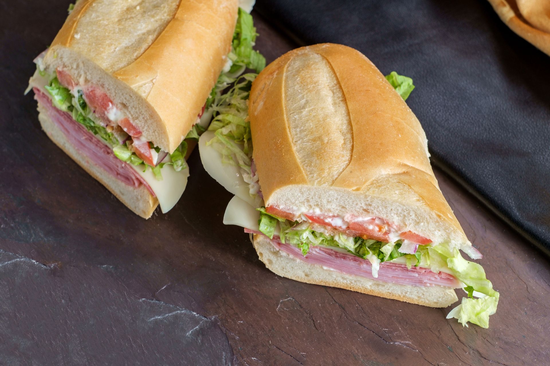 Two sub sandwiches are cut in half on a table.
