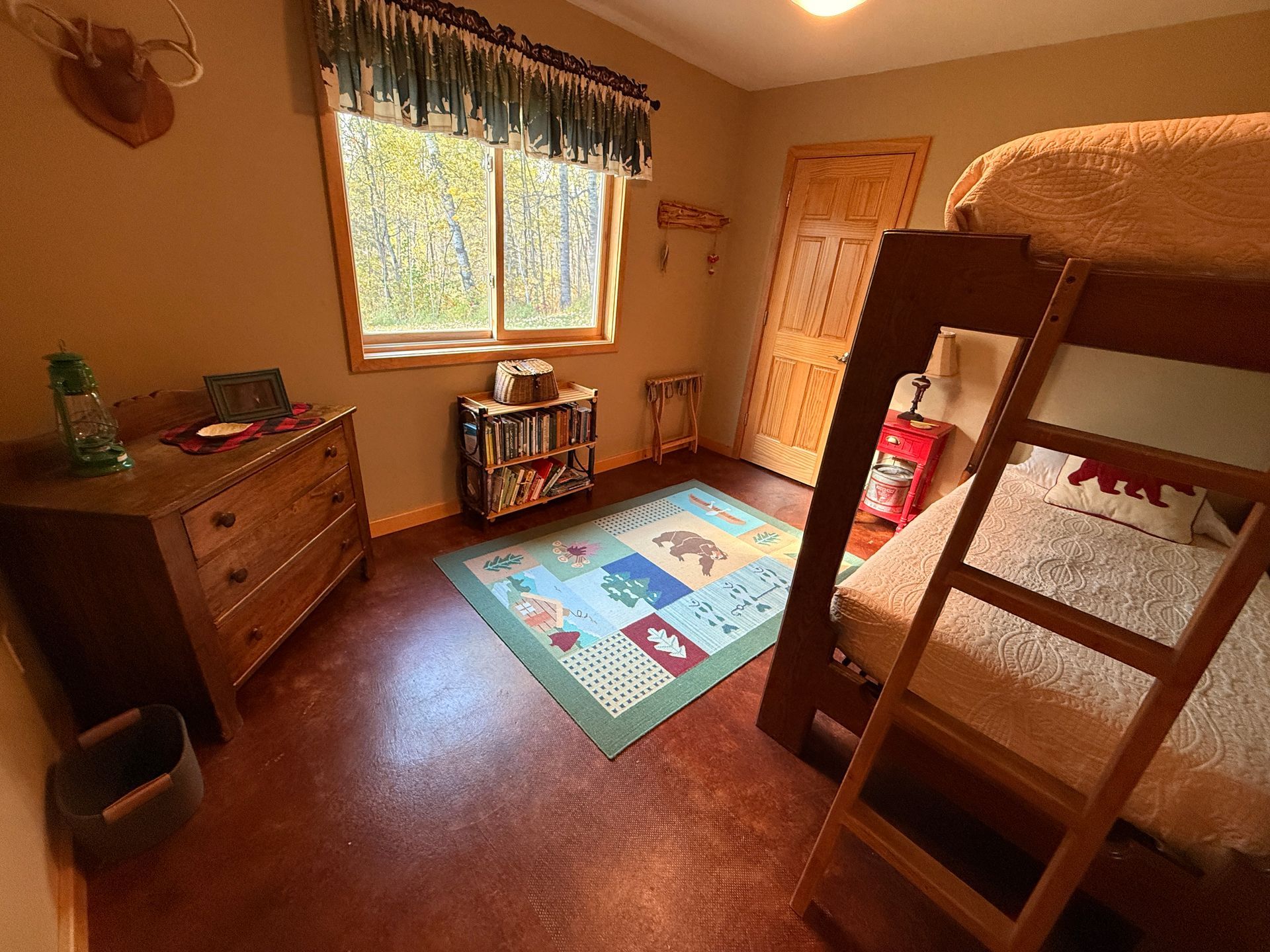 A bedroom with bunk beds , a rug , a dresser and a window.