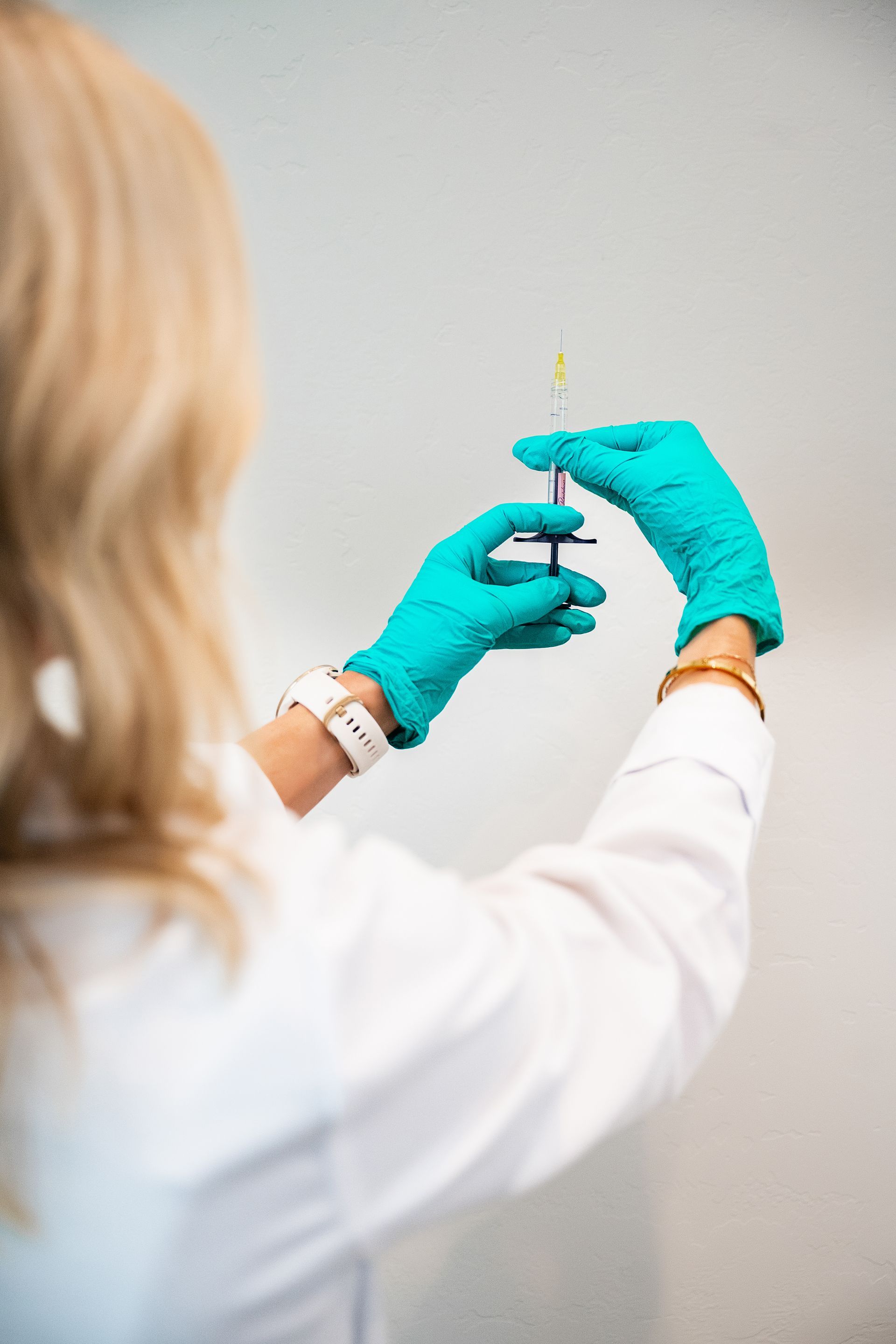 a woman in a lab coat and blue gloves is holding a syringe .