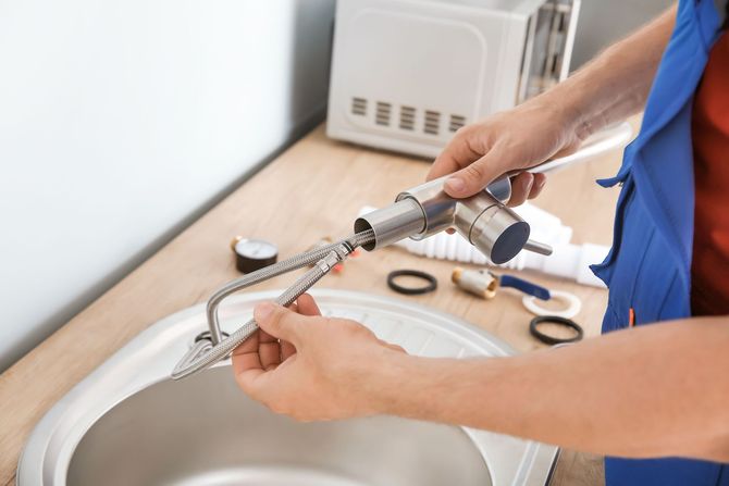 Hands using a handheld drill to work on a metal pipe over a sink
