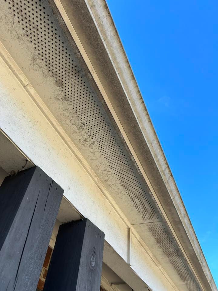 Close-up of a beige house eave with perforated soffit and dark wooden beams against blue sky