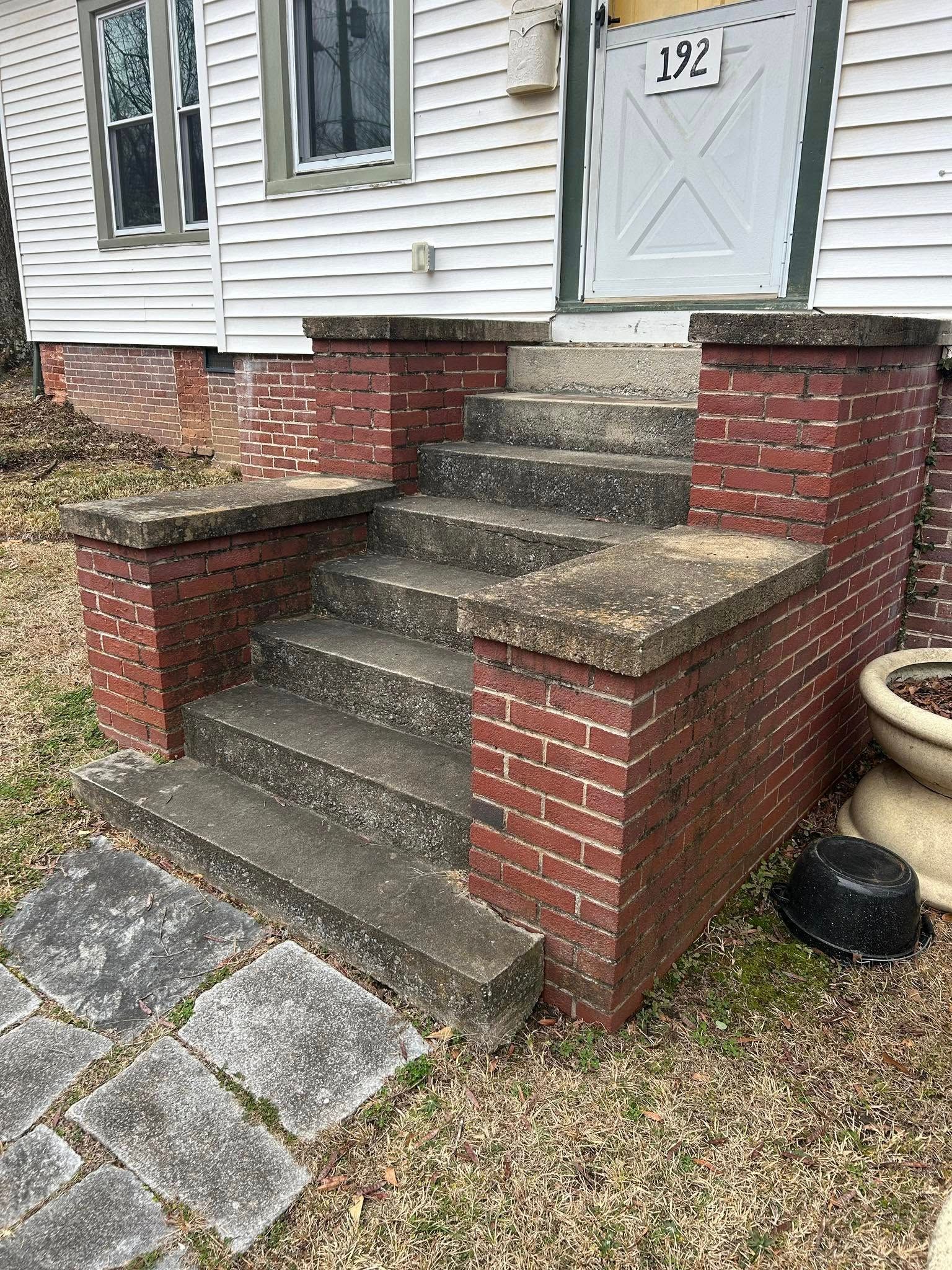 Front steps of a house with red brick walls, gray concrete stairs, and a white door numbered 192.