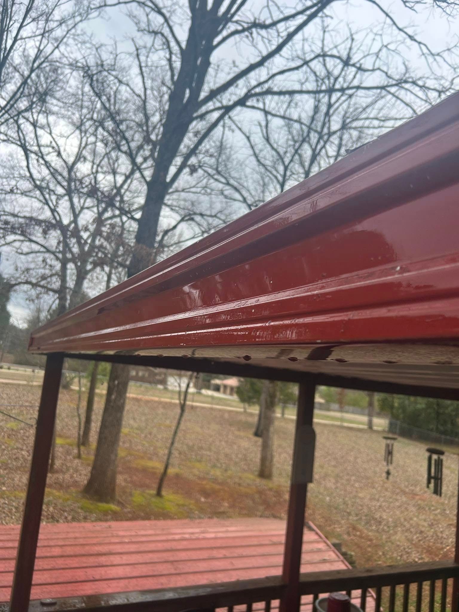 Red metal roof over a deck with leafless trees and a wooded yard in the background
